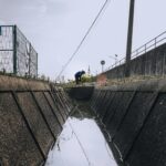 A person in blue attire working near a large drainage channel on a clear day.