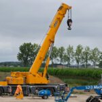 A large yellow crane at a construction site with lush greenery in the background.